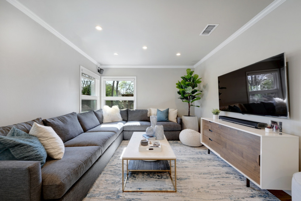 Modelo de salón abierto actual sin chimenea con paredes grises, suelo de madera en tonos medios, televisor colgado en la pared y suelo marrón