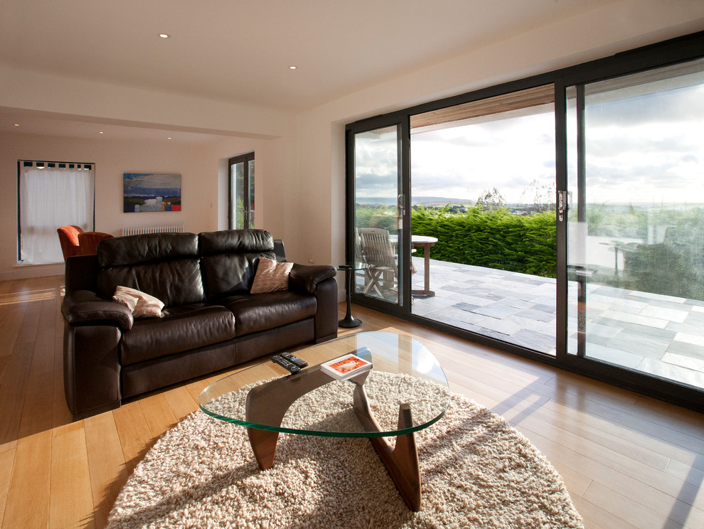 This is an example of a contemporary living room in Cornwall with white walls and light hardwood flooring.