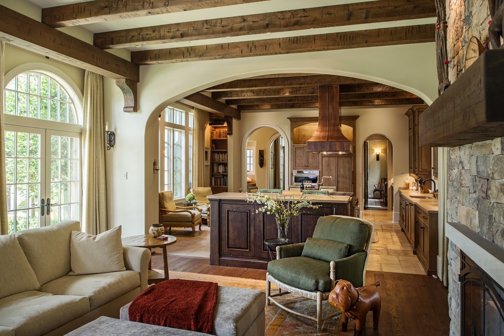 Example of a huge southwest open concept medium tone wood floor, brown floor and exposed beam living room design in Nashville with beige walls, a standard fireplace and a stone fireplace
