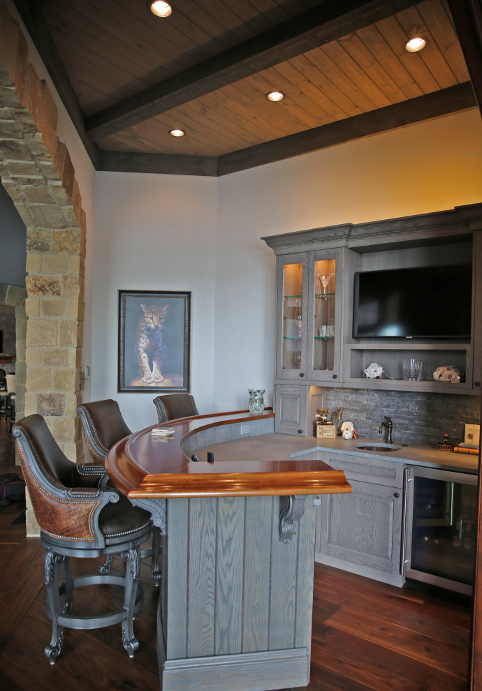 На фото: гостиная комната в стиле рустика с фасадом камина из камня, телевизором на стене, разноцветным полом и деревянным потолком