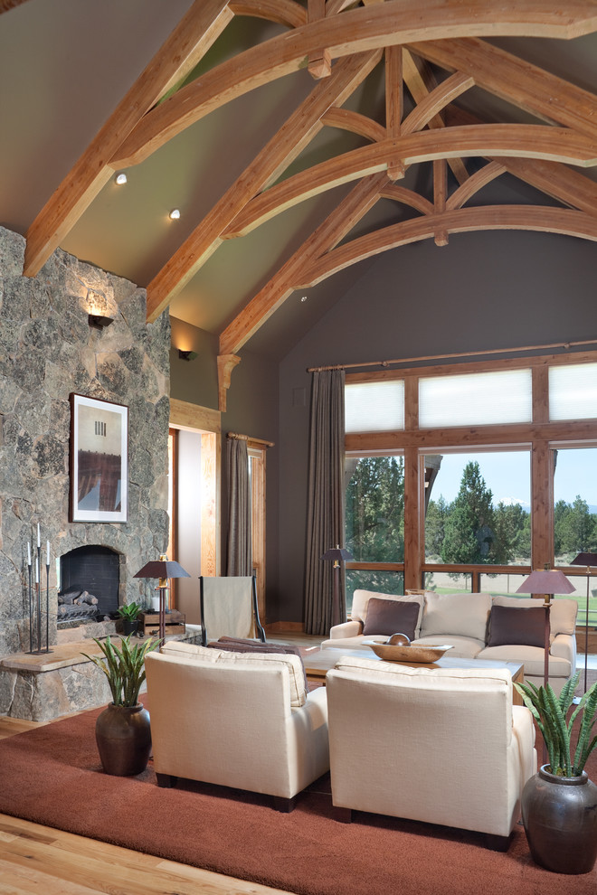 На фото: гостиная комната в стиле рустика с серыми стенами, стандартным камином, фасадом камина из камня и ковром на полу с