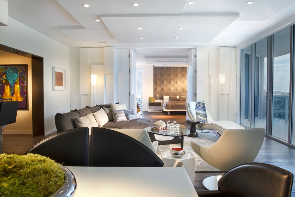На фото: гостиная комната в стиле модернизм с белыми стенами, темным паркетным полом и коричневым диваном с