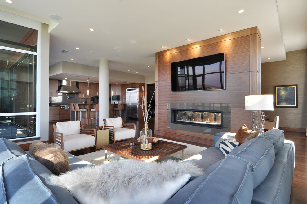 Design ideas for a medium sized contemporary open plan living room in Vancouver with medium hardwood flooring, a two-sided fireplace, a wooden fireplace surround and a wall mounted tv.