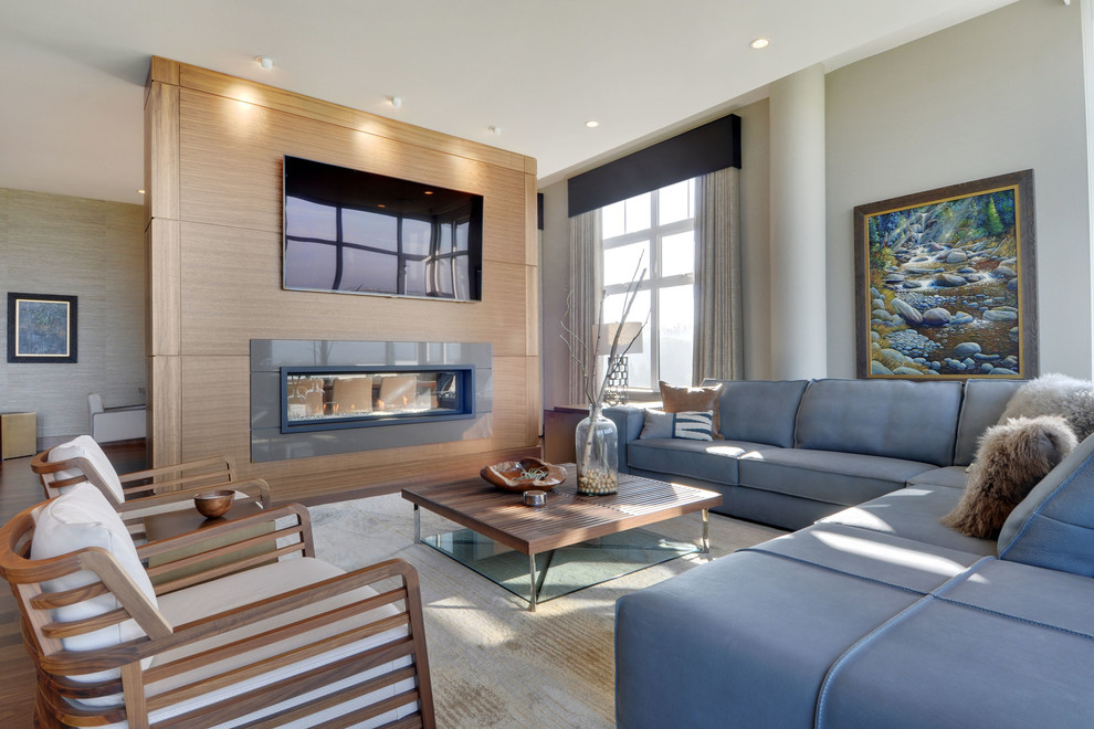 This is an example of a medium sized contemporary open plan living room in Vancouver with medium hardwood flooring, a two-sided fireplace, a wooden fireplace surround and a wall mounted tv.