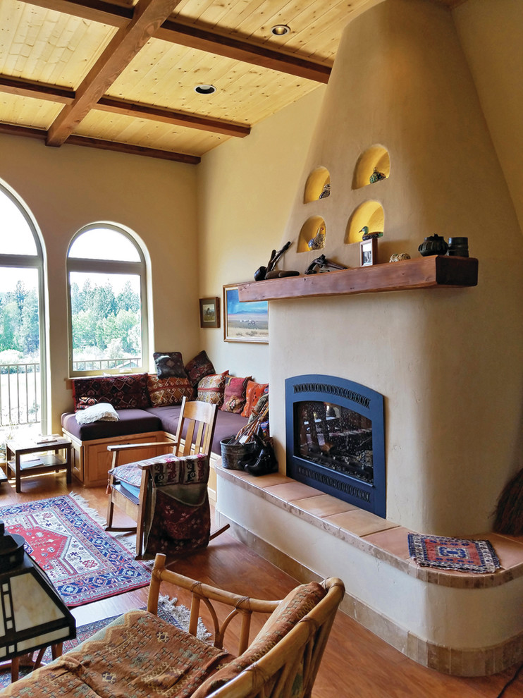 На фото: открытая гостиная комната среднего размера в стиле фьюжн с желтыми стенами, полом из ламината, стандартным камином и фасадом камина из штукатурки без телевизора