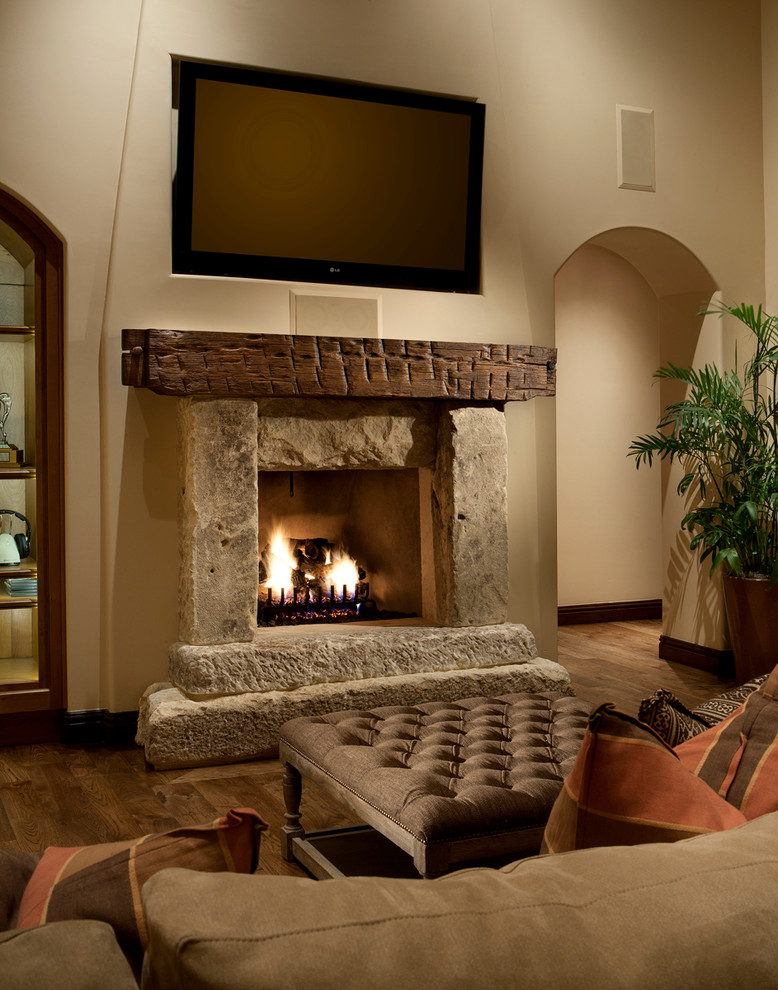 フェニックスにあるラグジュアリーな広い地中海スタイルのおしゃれなLDK (壁掛け型テレビ、ベージュの壁、標準型暖炉、石材の暖炉まわり、濃色無垢フローリング) の写真