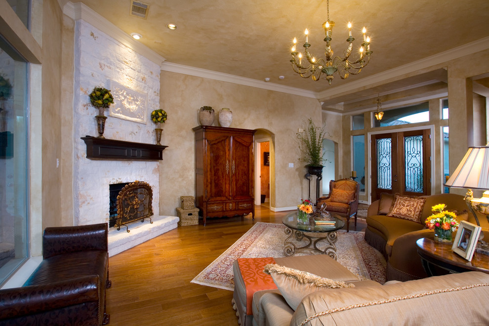Großes, Repräsentatives, Fernseherloses, Offenes Mediterranes Wohnzimmer mit beiger Wandfarbe, braunem Holzboden, Kamin und Kaminumrandung aus Stein in Austin