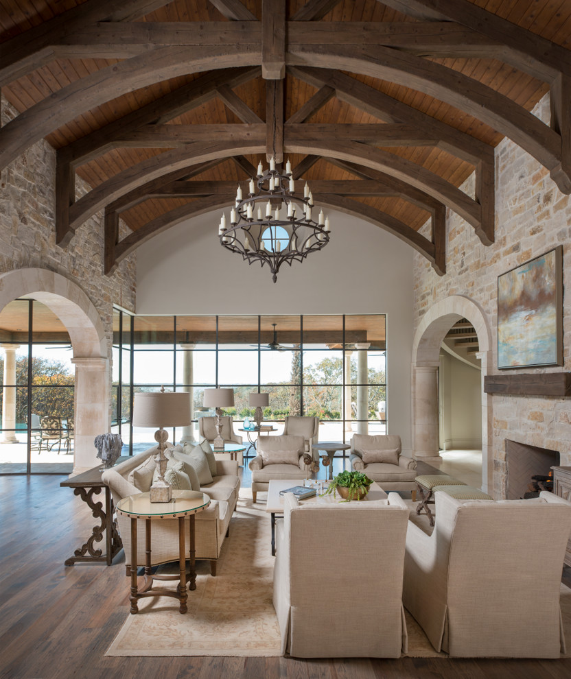Expansive mediterranean open plan living room in Dallas with medium hardwood flooring, a standard fireplace, a stone fireplace surround, brown floors and feature lighting.