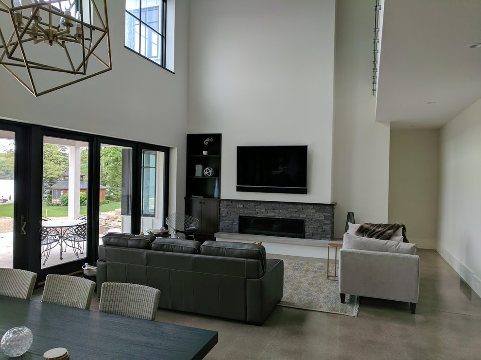 Стильный дизайн: изолированная гостиная комната среднего размера в классическом стиле с серыми стенами, бетонным полом, горизонтальным камином, фасадом камина из камня, телевизором на стене и серым полом - последний тренд