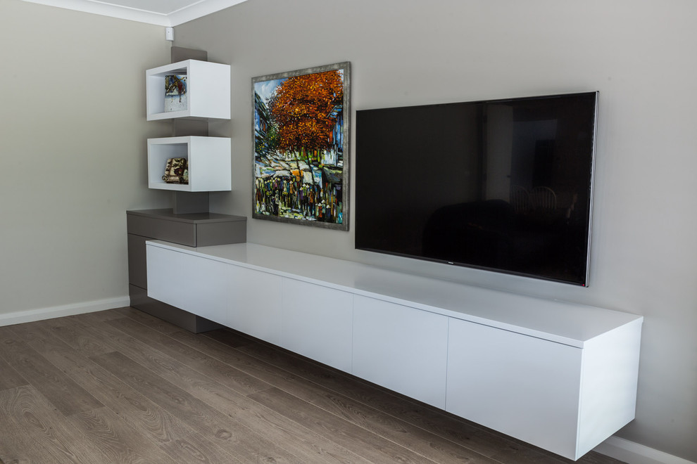 Cette image montre un grand salon minimaliste avec un mur beige, un sol en bois brun et un téléviseur fixé au mur.