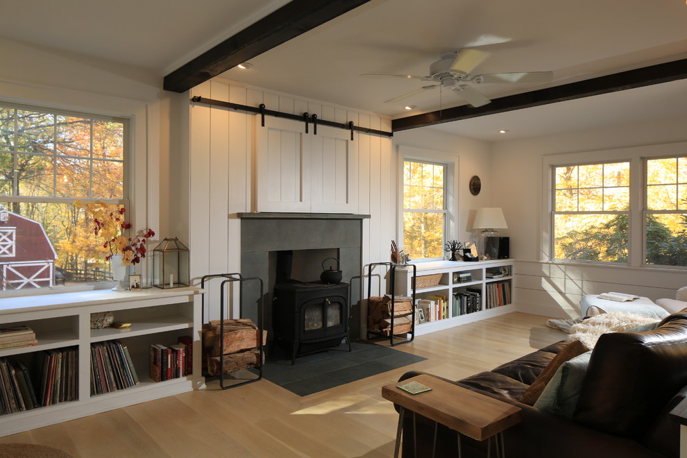Cette photo montre un salon chic avec un mur blanc, parquet clair, un poêle à bois, un manteau de cheminée en pierre et un téléviseur dissimulé.