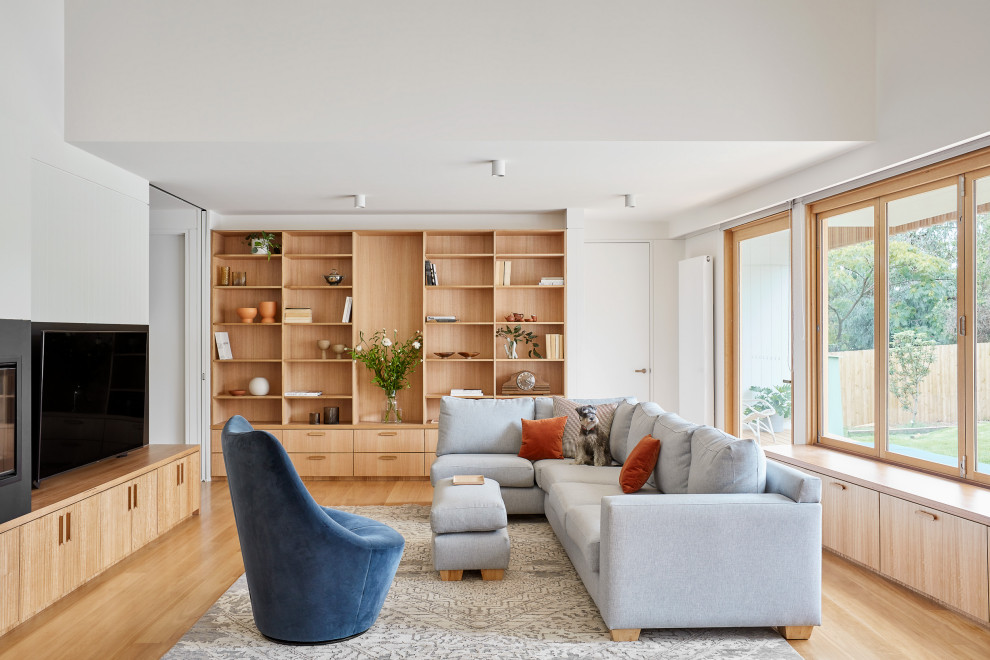 Imagen de salón cerrado actual grande con paredes blancas, suelo de madera clara, televisor independiente y suelo beige