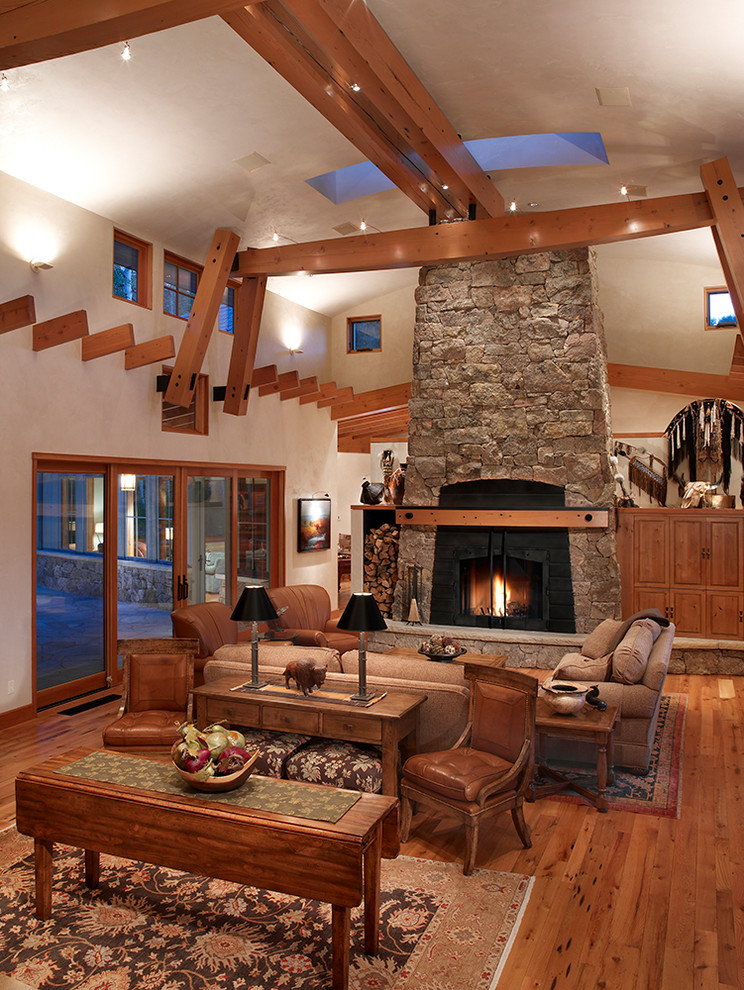 Large rustic open plan living room in Denver with beige walls, a standard fireplace, a stone fireplace surround and beige floors.