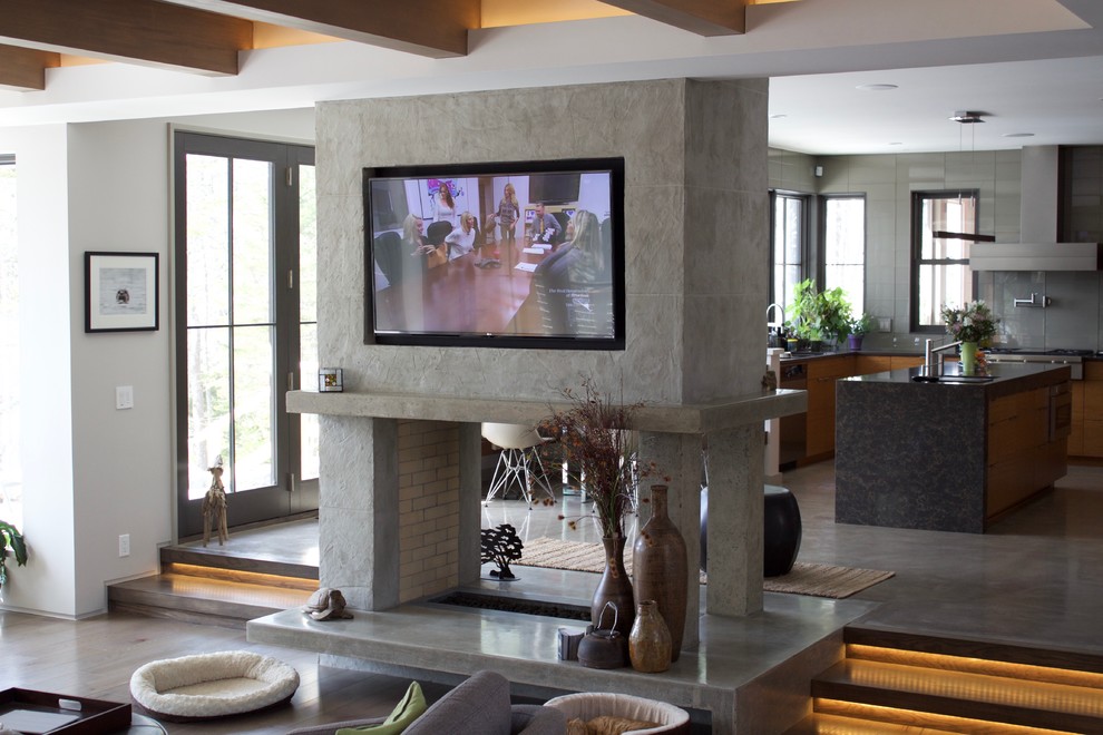 Ejemplo de salón abierto contemporáneo de tamaño medio con paredes grises, suelo de madera clara, chimenea de doble cara, marco de chimenea de yeso y televisor colgado en la pared