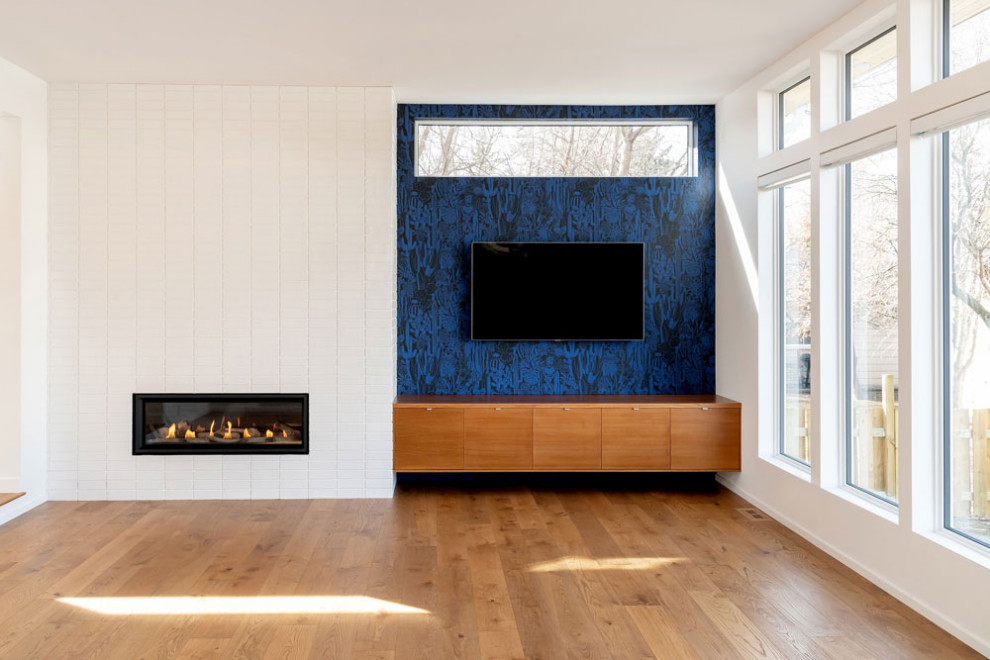 Offenes Retro Wohnzimmer mit weißer Wandfarbe, braunem Holzboden, Kamin, gefliester Kaminumrandung, Multimediawand und braunem Boden in Sonstige