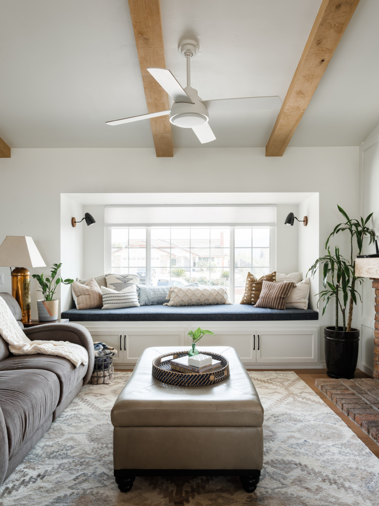 This is an example of a medium sized traditional open plan living room in San Diego with a reading nook, white walls, light hardwood flooring, a standard fireplace, a brick fireplace surround, a wall mounted tv, beige floors, exposed beams and panelled walls.