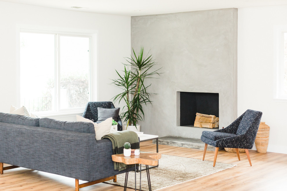 Cette image montre un salon design ouvert avec un manteau de cheminée en béton, une salle de réception, un mur blanc, parquet clair, une cheminée standard et un sol beige.