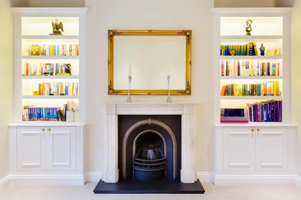 Living room library - traditional carpeted living room library idea in London with beige walls and a wood stove