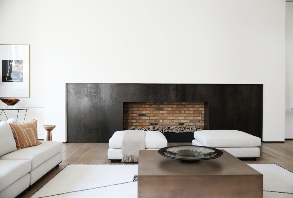 This is an example of a contemporary living room in London with white walls, medium hardwood flooring, a standard fireplace, a brick fireplace surround and brown floors.