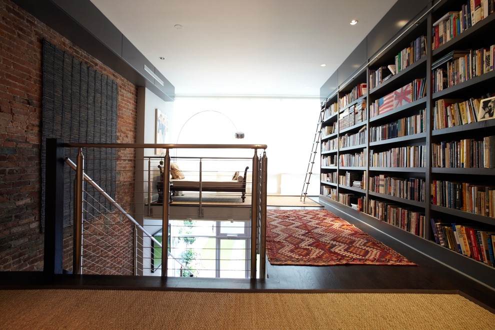 Imagen de biblioteca en casa abierta minimalista grande sin televisor con paredes grises, suelo de madera oscura, todas las chimeneas y marco de chimenea de piedra