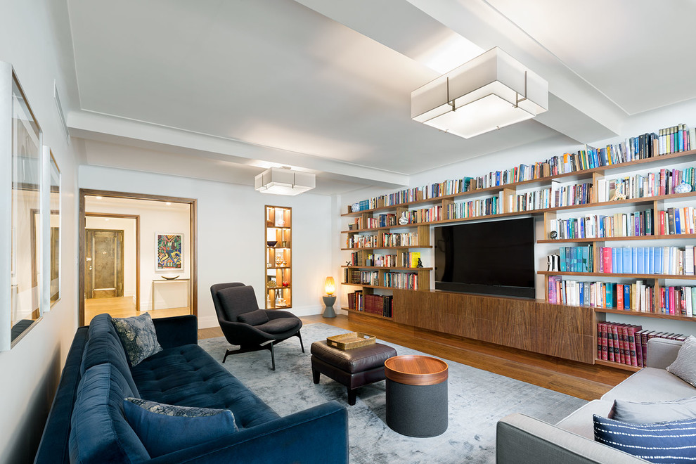 Modelo de biblioteca en casa cerrada actual grande sin chimenea con paredes blancas, suelo de madera en tonos medios y televisor colgado en la pared
