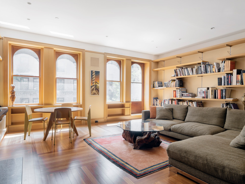 Offene Moderne Bibliothek ohne Kamin mit gelber Wandfarbe und braunem Holzboden in New York