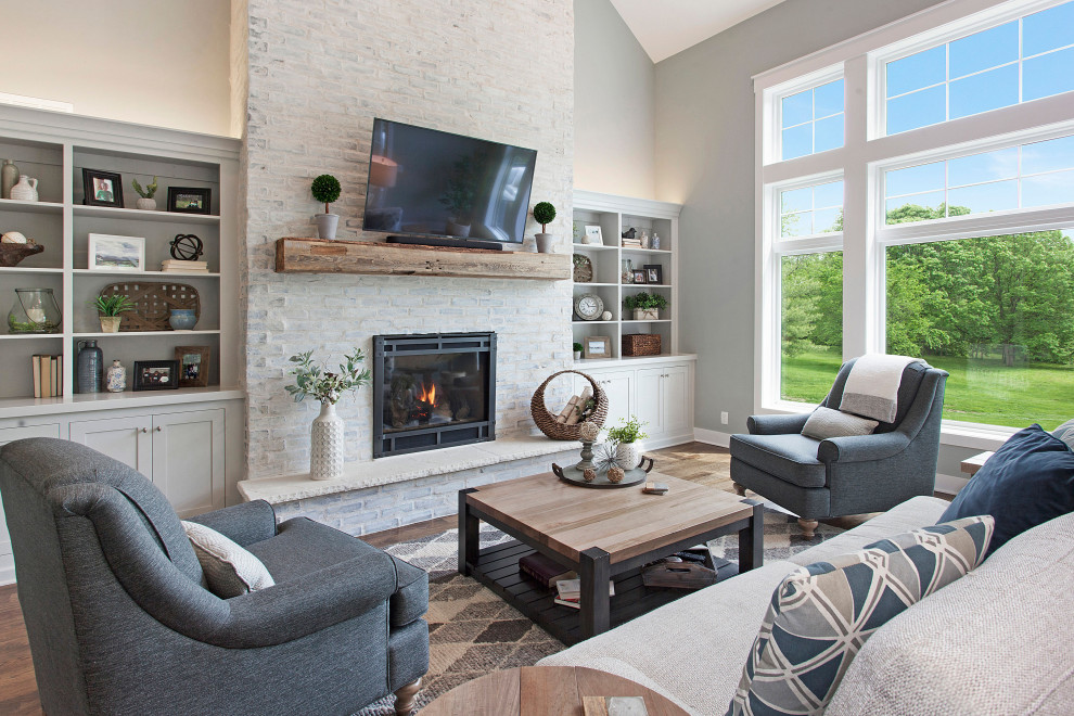 Inspiration for a mid-sized country medium tone wood floor and brown floor living room remodel in Kansas City with gray walls, a standard fireplace, a wall-mounted tv and a brick fireplace