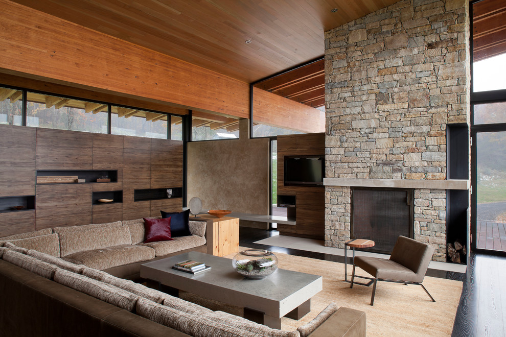 Expansive contemporary living room in New York with dark hardwood flooring, a standard fireplace, a stone fireplace surround, a wall mounted tv and beige walls.