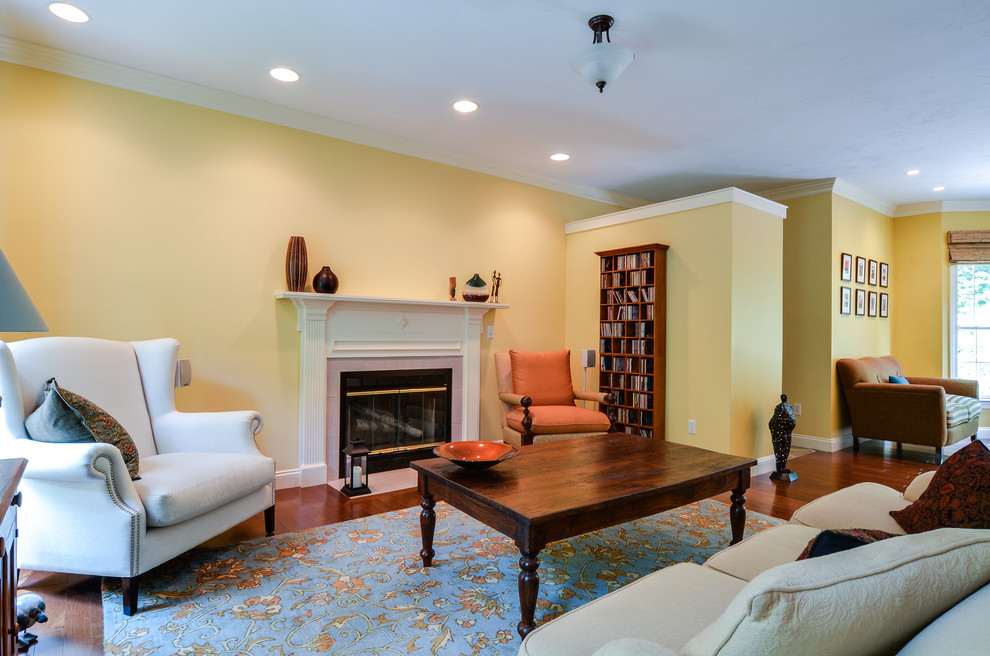 На фото: большая открытая гостиная комната в стиле неоклассика (современная классика) с с книжными шкафами и полками, желтыми стенами, паркетным полом среднего тона, стандартным камином и фасадом камина из дерева