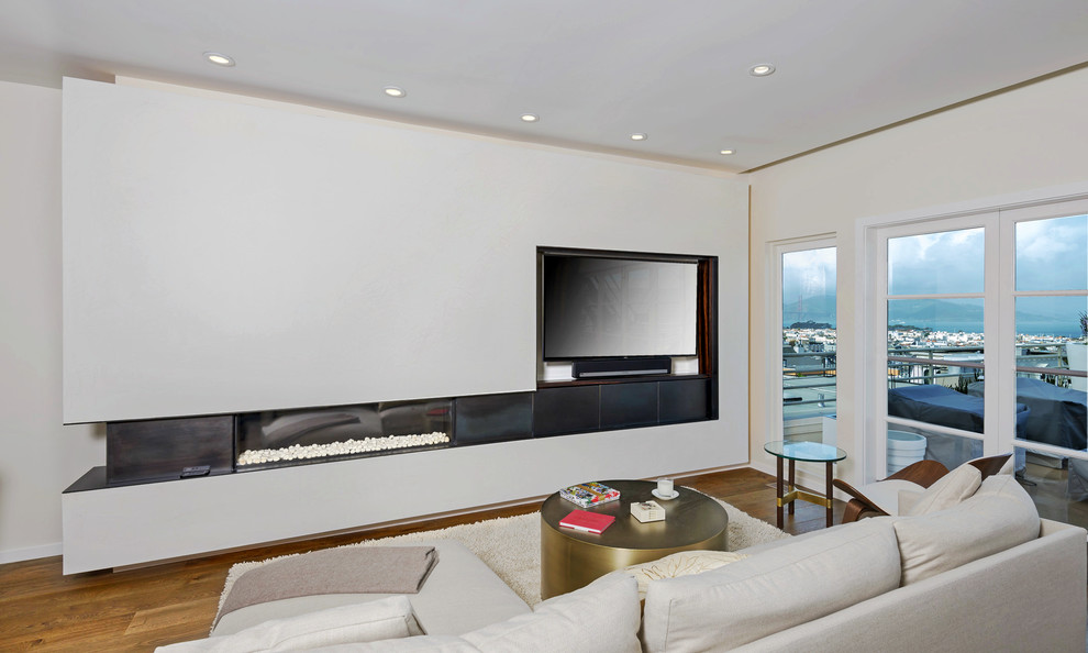Diseño de salón abierto contemporáneo grande con paredes blancas, suelo de madera en tonos medios, chimenea lineal, marco de chimenea de metal y televisor colgado en la pared