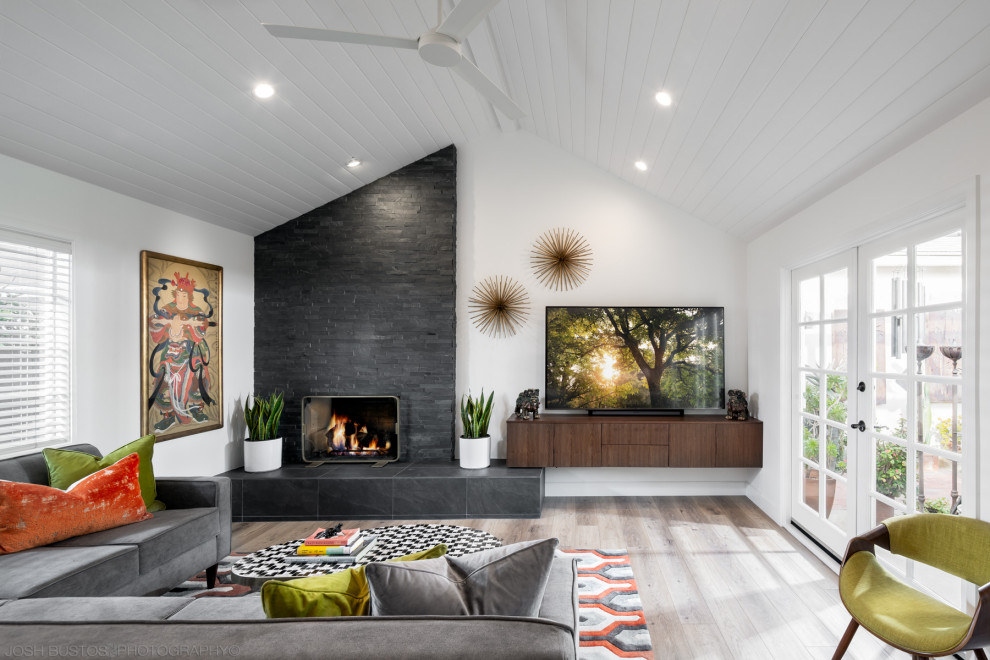 Cette photo montre un grand salon rétro ouvert avec un mur blanc, une cheminée standard, un manteau de cheminée en carrelage, un téléviseur indépendant, un sol gris et un plafond en lambris de bois.