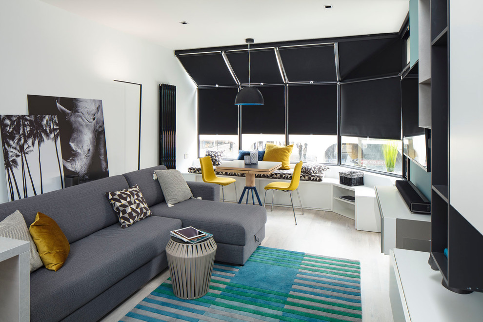 Medium sized contemporary grey and yellow open plan living room in Dublin with a reading nook, white walls, light hardwood flooring, a wall mounted tv and grey floors.