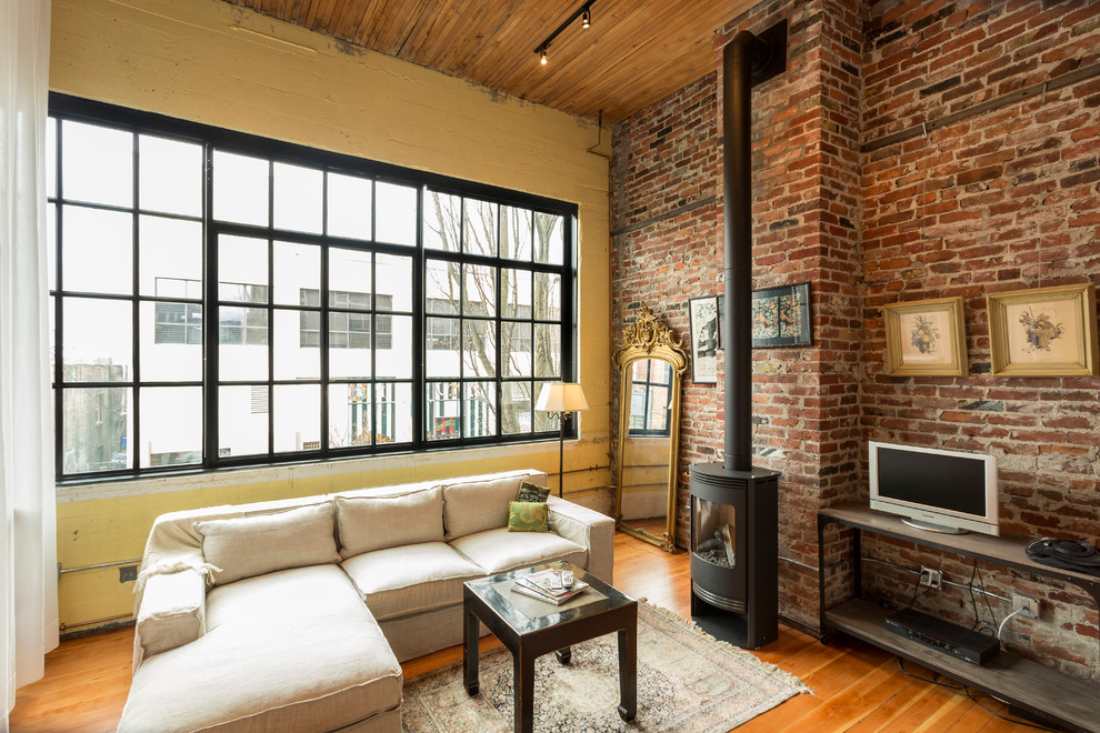 Immagine di un soggiorno industriale di medie dimensioni e aperto con pareti gialle, pavimento in legno massello medio, stufa a legna e TV autoportante