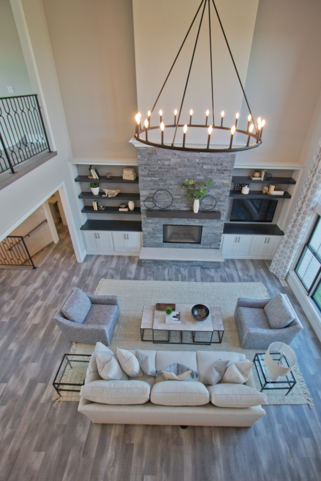 Large formal open plan living room with beige walls, vinyl flooring, a standard fireplace, a stacked stone fireplace surround, a corner tv, grey floors and a vaulted ceiling.
