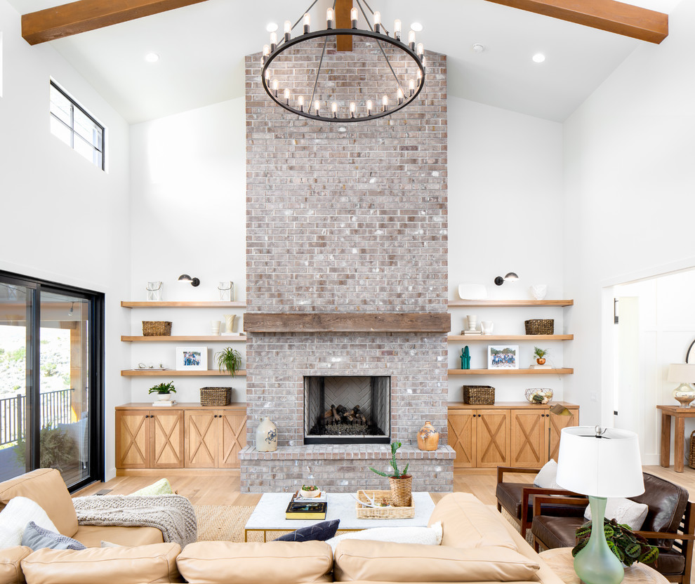 Large farmhouse formal open plan living room in Salt Lake City with white walls, light hardwood flooring, a standard fireplace, a brick fireplace surround, no tv, beige floors and feature lighting.