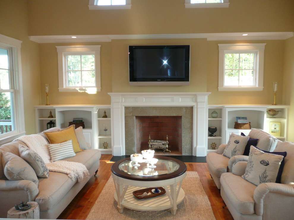 Пример оригинального дизайна: большая открытая гостиная комната в стиле неоклассика (современная классика) с желтыми стенами, паркетным полом среднего тона, стандартным камином, фасадом камина из дерева и телевизором на стене