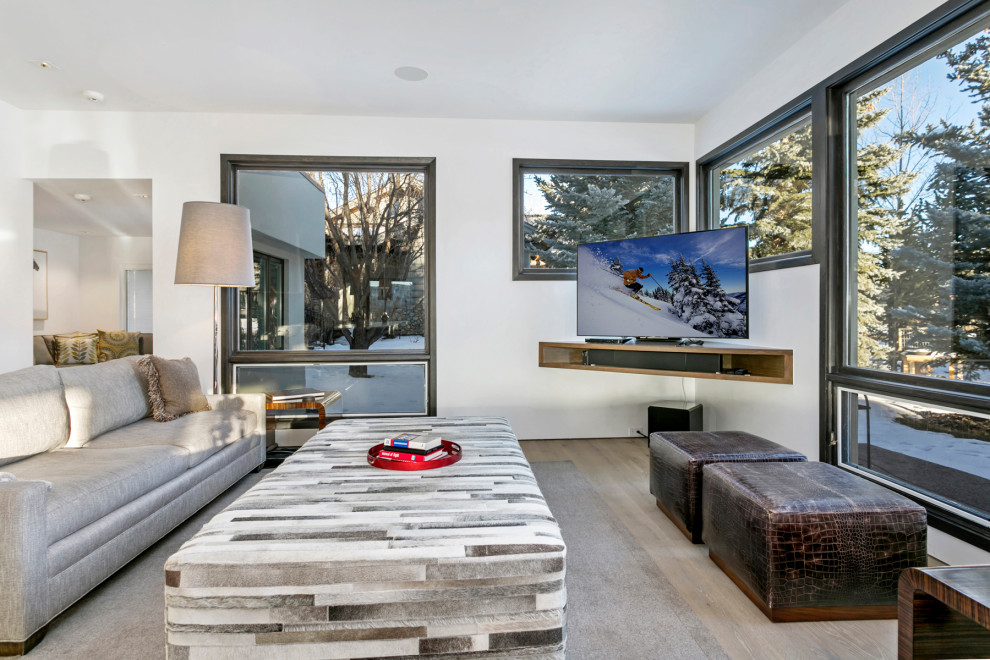 На фото: большая открытая гостиная комната в стиле модернизм с белыми стенами, светлым паркетным полом, телевизором в углу, коричневым полом и многоуровневым потолком