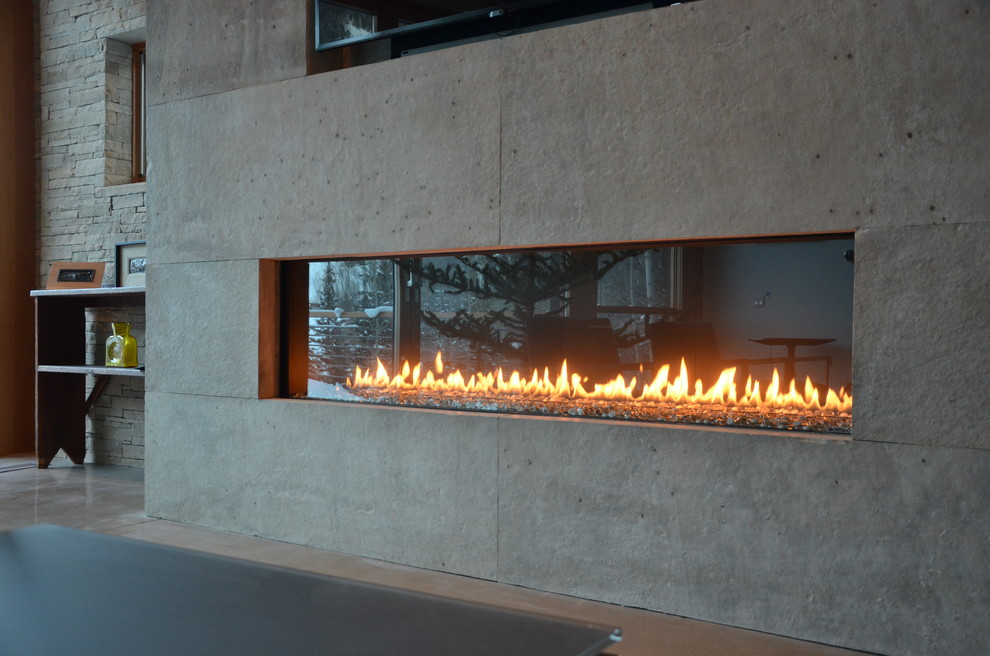 デンバーにある広いコンテンポラリースタイルのおしゃれなリビング (ベージュの壁、コンクリートの床、横長型暖炉、石材の暖炉まわり、埋込式メディアウォール) の写真