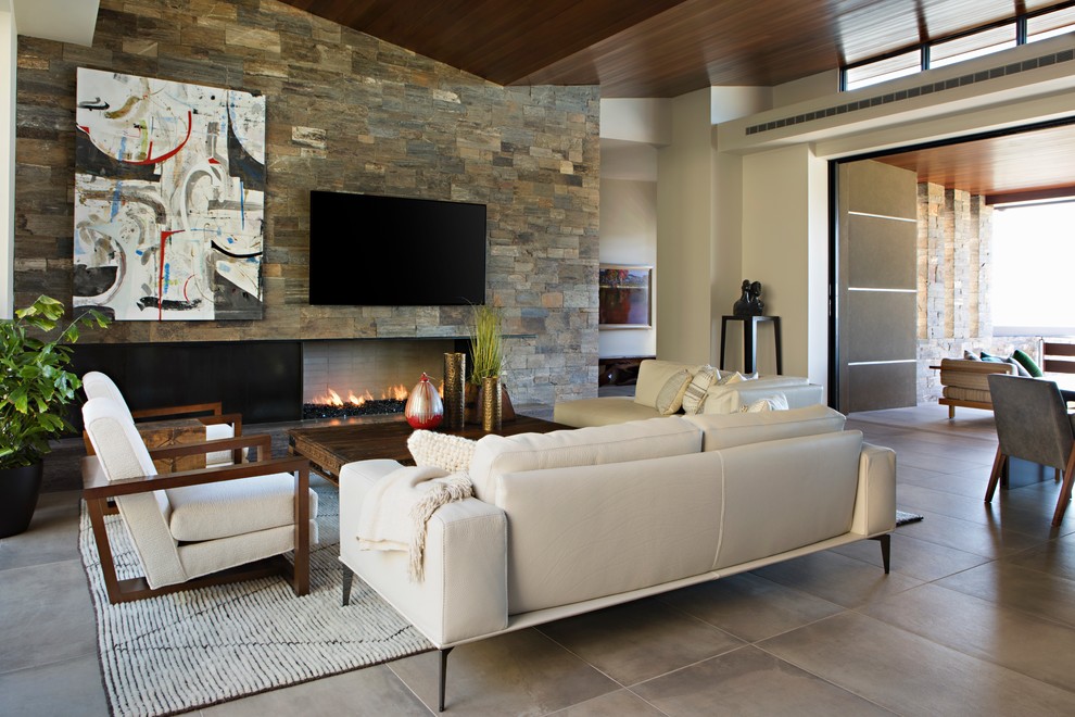 Стильный дизайн: большая парадная, открытая гостиная комната в стиле модернизм с коричневыми стенами, полом из известняка, горизонтальным камином, фасадом камина из камня, телевизором на стене и бежевым полом - последний тренд