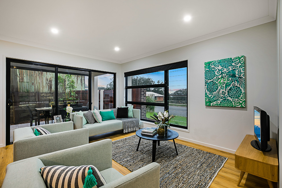 Offenes Modernes Wohnzimmer ohne Kamin mit weißer Wandfarbe, braunem Holzboden und freistehendem TV in Brisbane