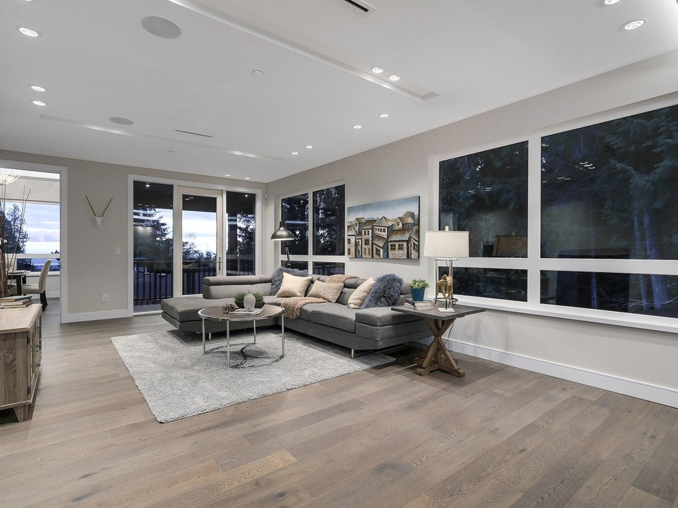 This is an example of a medium sized contemporary open plan living room in Vancouver with grey walls, light hardwood flooring, a standard fireplace, a stone fireplace surround, a freestanding tv and beige floors.