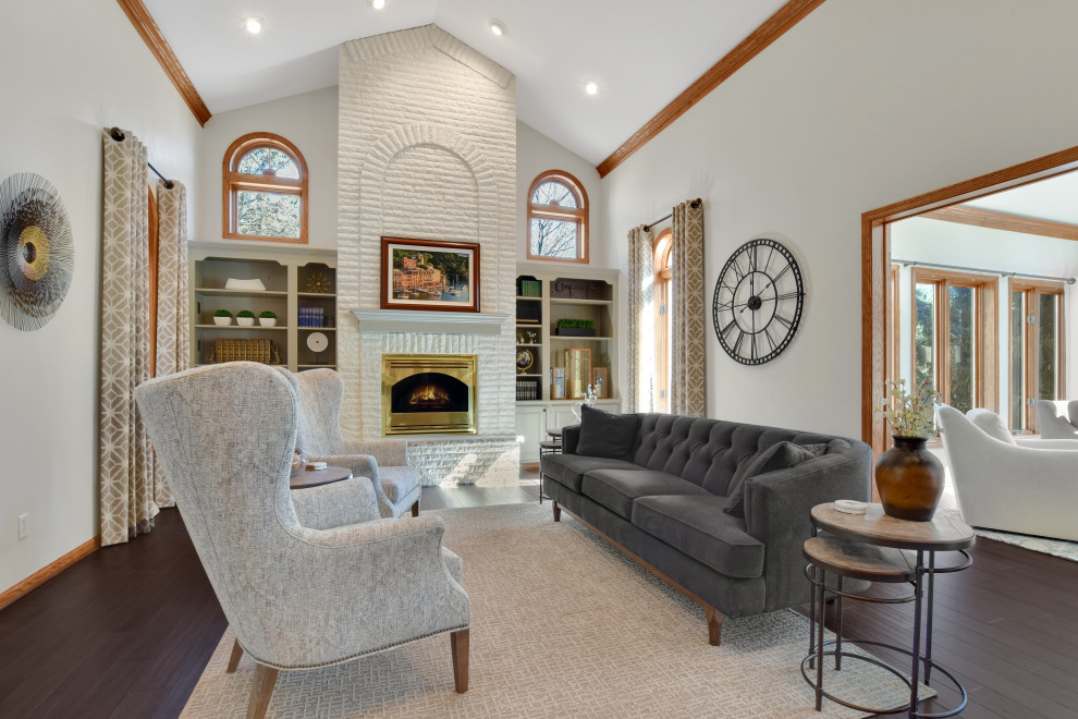 Cette photo montre un grand salon chic ouvert avec un mur gris, parquet foncé, une cheminée standard, un manteau de cheminée en brique et un sol marron.