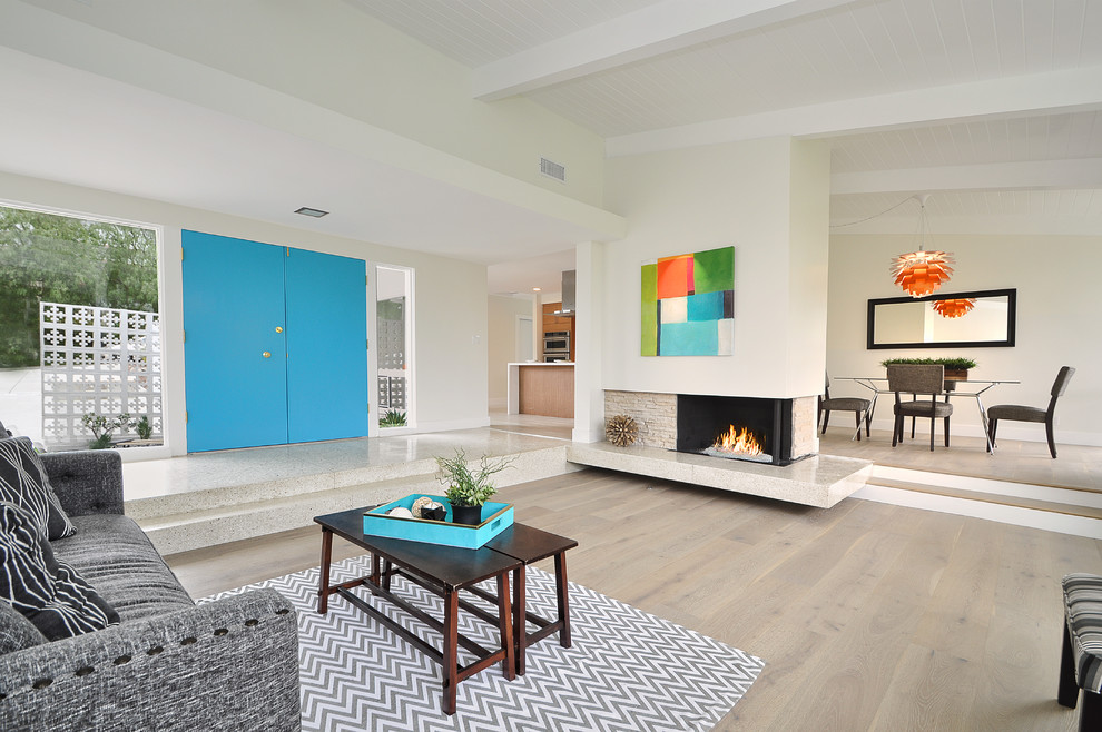 This is an example of a retro grey and teal open plan living room in Los Angeles with white walls, light hardwood flooring, beige floors, a standard fireplace and a stone fireplace surround.