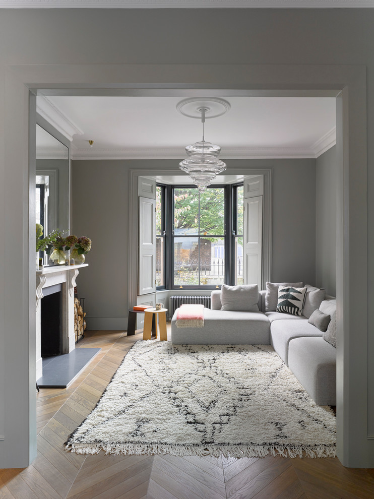 Mittelgroßes, Abgetrenntes Modernes Wohnzimmer mit grauer Wandfarbe, hellem Holzboden, Kamin, Kaminumrandung aus Stein und braunem Boden in London