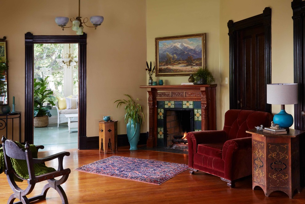 Пример оригинального дизайна: парадная гостиная комната в викторианском стиле с желтыми стенами, светлым паркетным полом, угловым камином и фасадом камина из дерева без телевизора