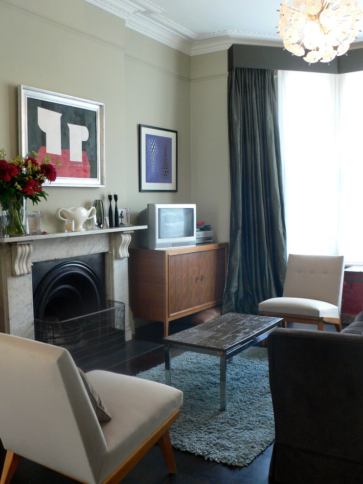 Klassisches Wohnzimmer mit grüner Wandfarbe, dunklem Holzboden, Kamin, Kaminumrandung aus Stein und freistehendem TV in London