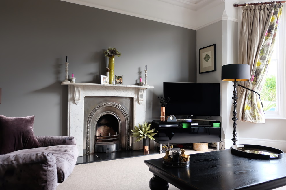 Medium sized victorian enclosed living room in Other with grey walls, carpet, a standard fireplace, a stone fireplace surround, a freestanding tv and beige floors.