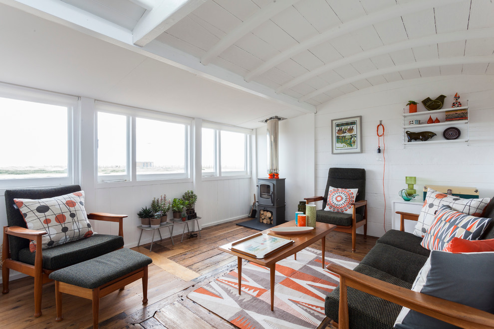 На фото: гостиная комната в скандинавском стиле с белыми стенами, паркетным полом среднего тона и печью-буржуйкой