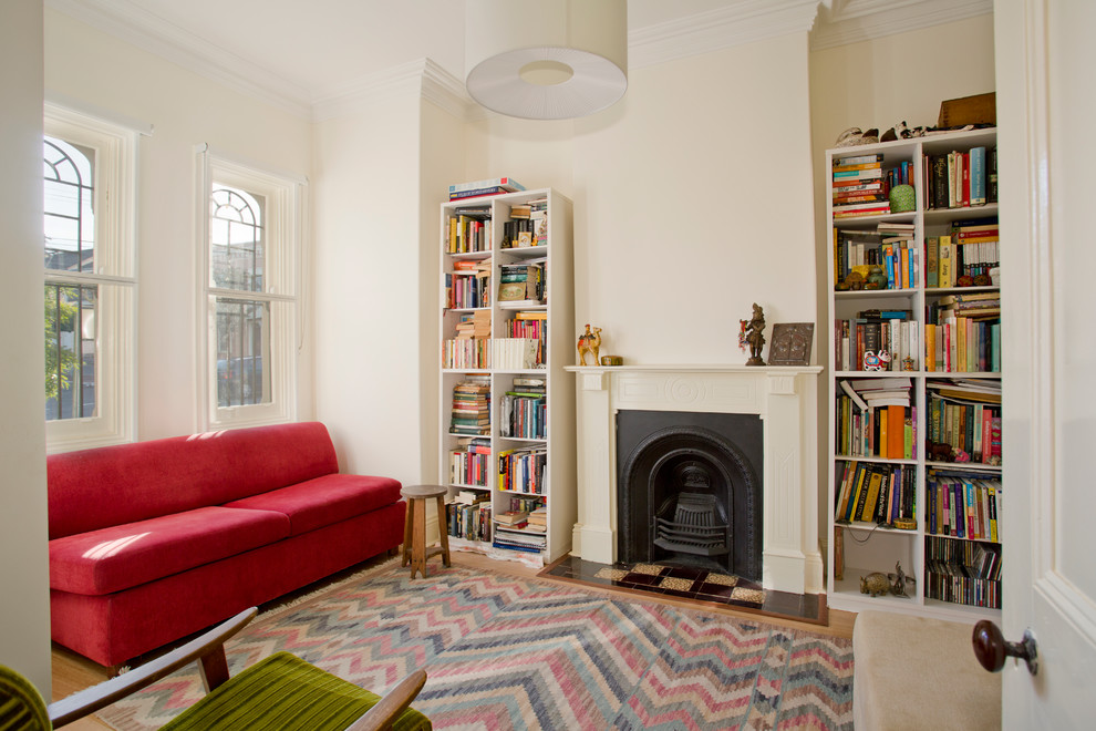 Exempel på ett litet klassiskt separat vardagsrum, med ett bibliotek, en standard öppen spis, vita väggar, ljust trägolv och en spiselkrans i gips