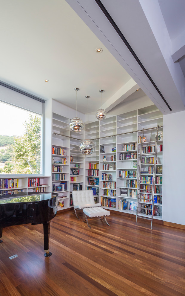 Idéer för att renovera ett mellanstort funkis allrum med öppen planlösning, med ett bibliotek, vita väggar, mellanmörkt trägolv och brunt golv